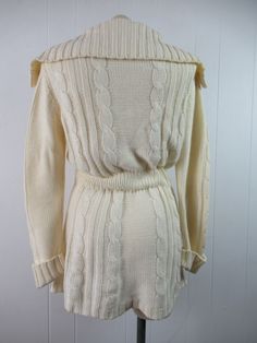 "Vintage 1970s sweater. Made of Acrylic knit. Color is cream white. Bohemian hippy style. Has a button down front, wooden buttons, large cowl style collar, internal cinches waist belt and two lower pockets. Made by F.O.B./ N.Y. About a size medium. Actual measurements are: 36\" at the bust 29\" at the waist 39\" at the hips 15.5\" shoulder seam to shoulder seam 28\" shoulder seam to cuff(with cuffs not rolled up) 33\" overall length In excellent condition." Long Fitted Cream Sweater, Vintage Knit Sweater Coat With Long Sleeves, Vintage Knit Sweater Coat, Vintage Knitted Sweater Coat With Long Sleeves, Vintage Knitted Long Sleeve Sweater Coat, Vintage Cream Long Sleeve Cardigan, Fitted Vintage Sweater Coat With Long Sleeves, Fitted Long Sleeve Vintage Sweater Coat, Vintage Cream Sweater For Fall