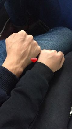 two people holding hands while sitting on a bus seat with the seats down and one person wearing a red heart bracelet