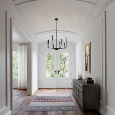 a hallway with white walls and wooden floors has a chandelier hanging from the ceiling