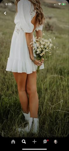 a woman standing in tall grass holding a bouquet of flowers and looking at the sky