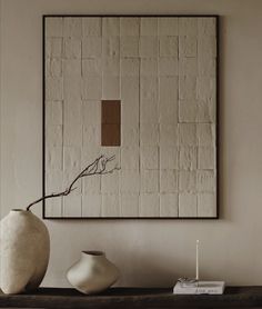 a white vase sitting on top of a wooden table next to a framed piece of art