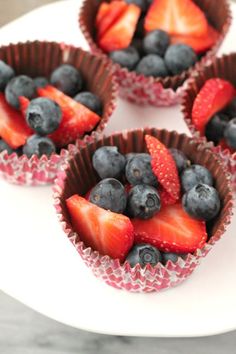 four chocolate cups filled with fruit on top of a white plate and sitting on a table