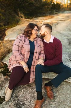 a man and woman sitting on top of a rock next to each other, smiling