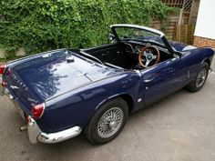 an old blue sports car parked in front of a house