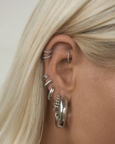 a woman with blonde hair wearing three silver rings and two star ear cuff earrings on her left ear