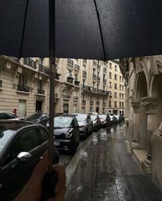 a person holding an umbrella on a rainy day in the city with cars parked along the street