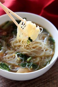 a white bowl filled with noodles and vegetables on top of a table next to chopsticks