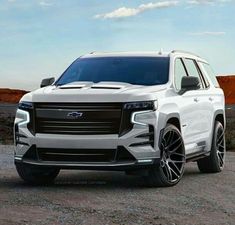 the front end of a white suv parked on top of a dirt field