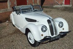 an old white car parked in front of a brick building