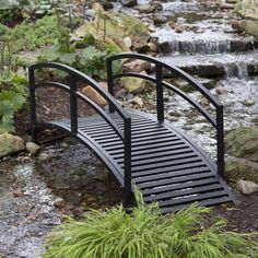 a small bridge over a stream in the middle of a forest with rocks and plants