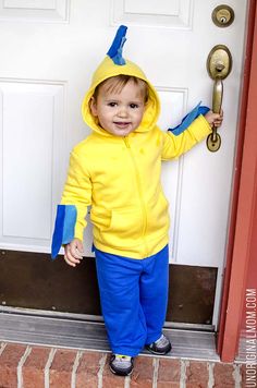 a little boy in a yellow and blue costume standing by a door with his hand on the handle