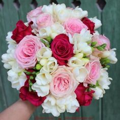 a bridal bouquet with pink and white flowers in front of a green fenced area