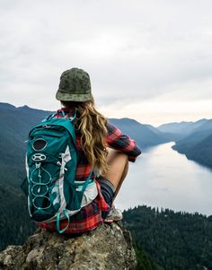 a woman sitting on top of a mountain looking out over the water and mountains in the distance