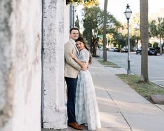 a man and woman standing next to each other on the sidewalk near a building with palm trees