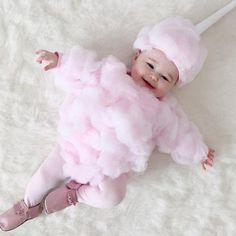 a baby wearing a pink dress and headband laying on a white blanket with her arms out