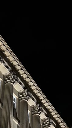 a clock on the side of a tall building at night with columns and lights around it