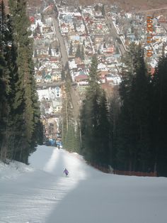 a person riding skis down a snow covered slope in front of a small town