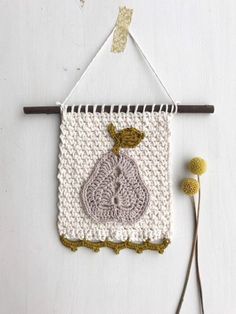 a crocheted wall hanging on a white wall next to two yellow and brown flowers