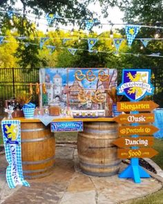 an outdoor bar set up with wooden barrels and signs on the outside, along with bunting streamers