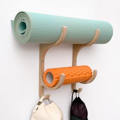 an orange yoga mat hanging on a wall next to two bags and a bag holder