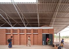 some people are standing in front of a red brick building with metal roof and doors