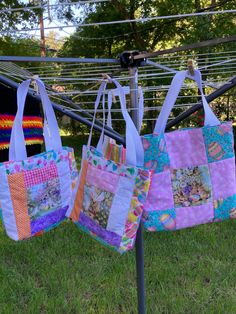 three bags are hanging on a clothesline outside in the grass, with trees in the background