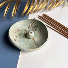 a green bowl sitting on top of a table next to some sticks and a plant