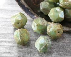 several green beads sitting on top of a wooden table next to a bowl filled with leaves