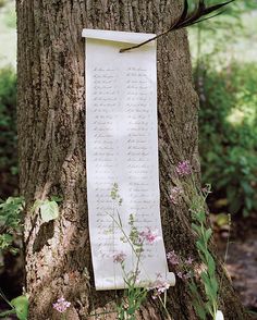 a paper hanging on the side of a tree with writing on it and flowers growing around