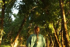 a woman is walking through the woods with her back turned to the camera and looking at trees