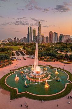 an aerial view of a fountain in the middle of a park with skyscrapers in the background