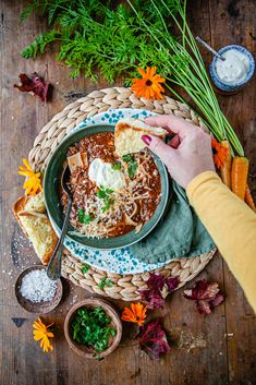 a bowl of soup is being served on a table with carrots, bread and flowers