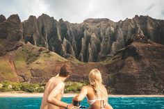 two people sitting on the back of a boat looking out at mountains and water in front of them