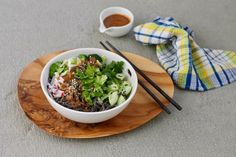 a bowl of food with chopsticks and sauce on a wooden plate next to a napkin