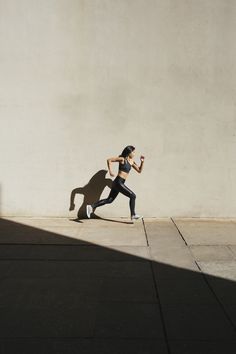 a woman running down the street in front of a wall with her shadow on it