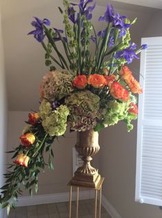 a vase filled with lots of flowers sitting on top of a wooden stand next to a window