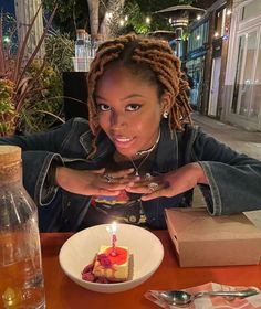 a woman sitting at a table with a piece of cake in front of her and a lit candle on the plate