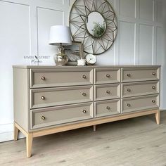 a dresser with several drawers and a lamp on top of it in front of a white wall