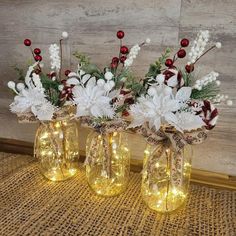 three glass vases with flowers and lights in them on a tablecloth covered floor