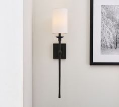 a wall mounted light with a white shade on it's side next to a framed photograph