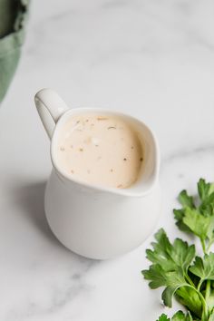 a cup of soup with parsley next to it on a marble counter top,