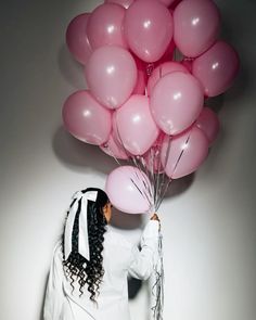 a woman holding pink balloons in her hand and wearing a white jacket with black stripes