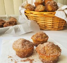 three sugared donuts sitting on top of a napkin next to a basket of doughnuts