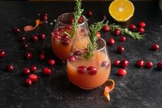 two glasses filled with drinks sitting on top of a table next to cranberries