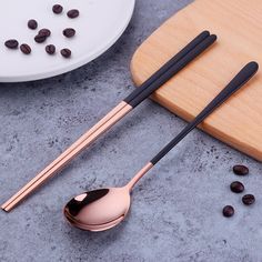 two spoons with black handles are next to coffee beans