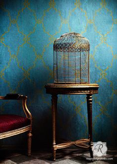 a bird cage sitting on top of a wooden table next to a red chair in front of a blue wall