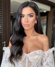 a woman with long black hair wearing a white top and earrings is looking at the camera