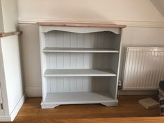 a white book shelf in the corner of a room next to a radiator