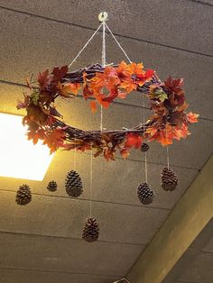 a wreath hanging from the ceiling with pineconis and autumn leaves on it's hanger