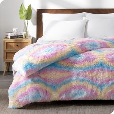 a bed with a colorful blanket on top of it next to a night stand and nightstand